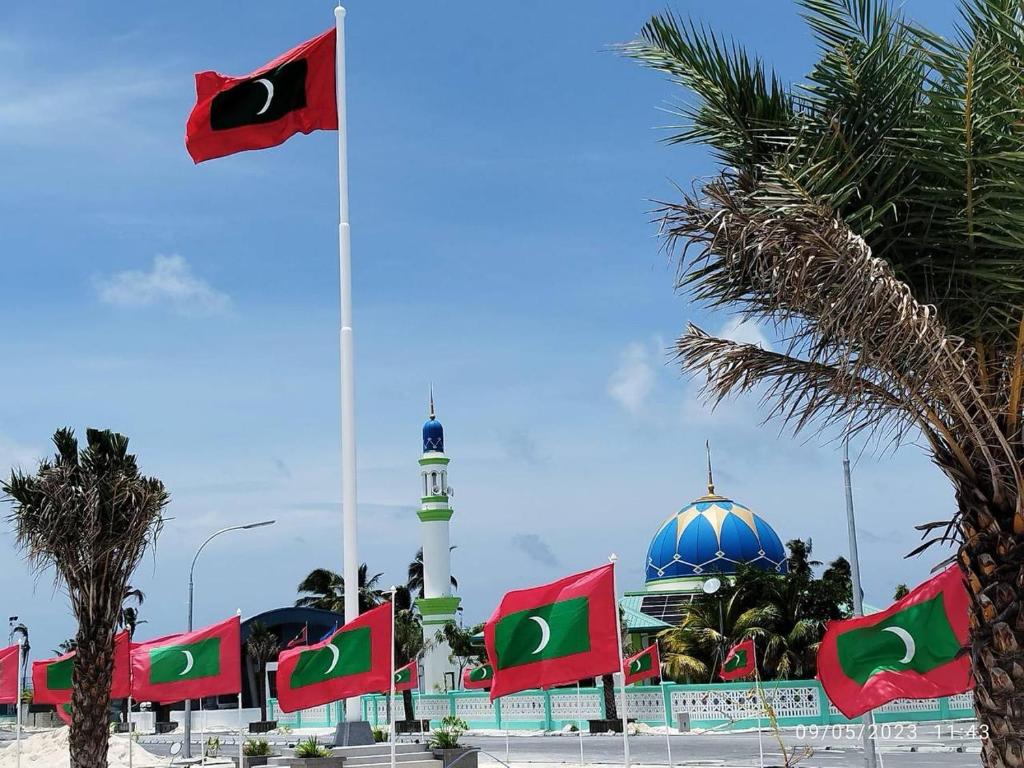 a mosque with a flag in front of it with palm trees at Aanirustayinn in Hoarafushi