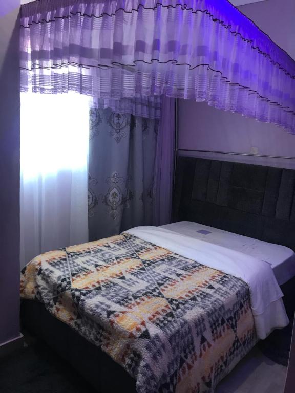 a bedroom with a bed with purple curtains and a window at Christine's Airbnb in Mbale