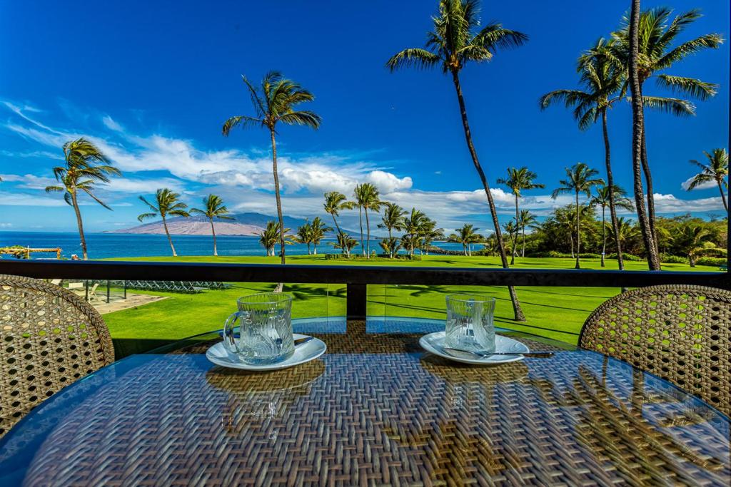 a table with a view of the ocean and palm trees at Enjoy Your Oceanside Dream at Kihei Surfside in Wailea