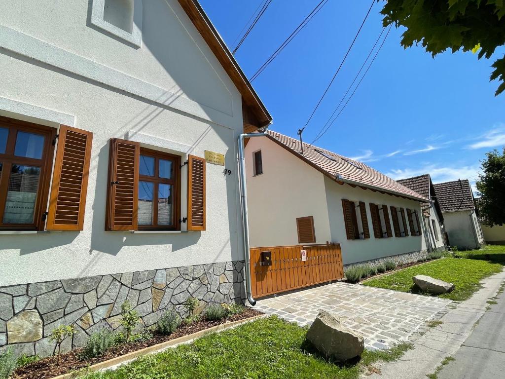 a white house with wooden windows and a stone wall at Kis-Duna Vendégház in Dunabogdány