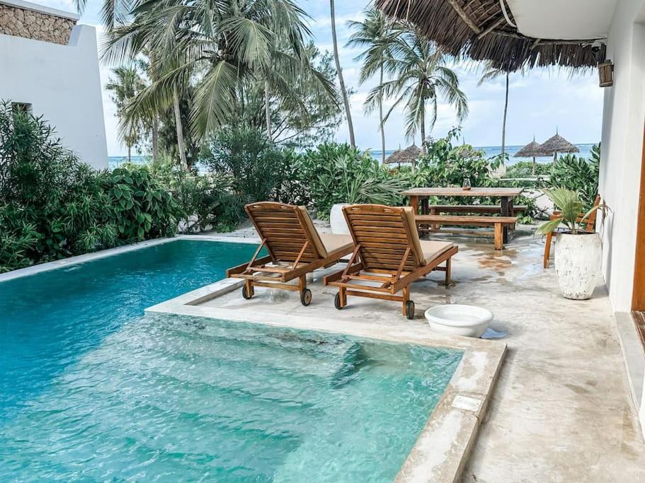 two chairs and a table next to a swimming pool at Villa Upendo with pool, Zanzibar in Pingwe