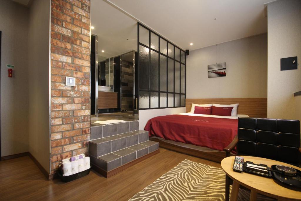 1 dormitorio con cama roja y pared de ladrillo en The May Hotel en Busan