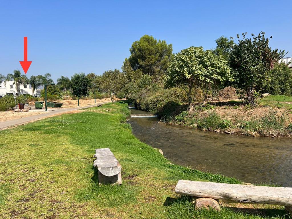 a river with a bench in the grass next to a road at שפיגל קו ראשון לנחל-Hagoshrim,הגושרים in Hagoshrim
