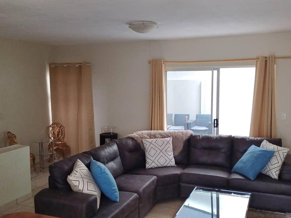 una sala de estar con un sofá de cuero marrón con almohadas azules en ABSOLUTE AIRBNB en Windhoek