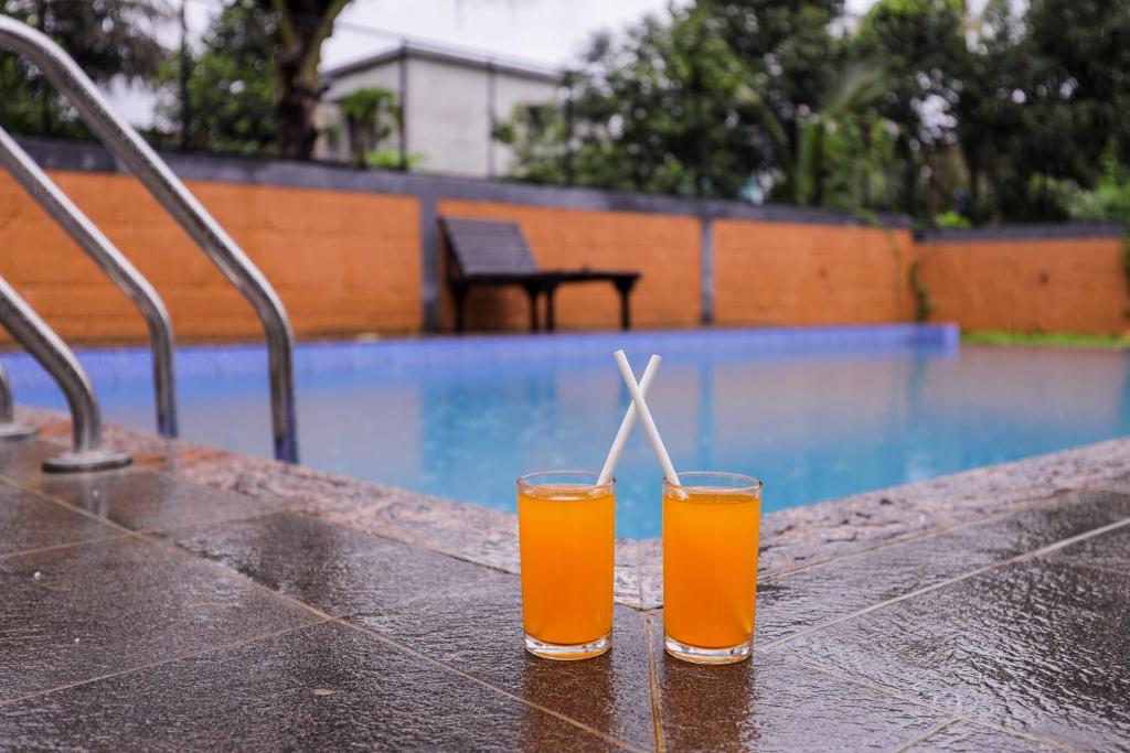 two glasses of orange juice sitting on a table near a swimming pool at SKY BLUE HOMESTAY with POOL in Vythiri