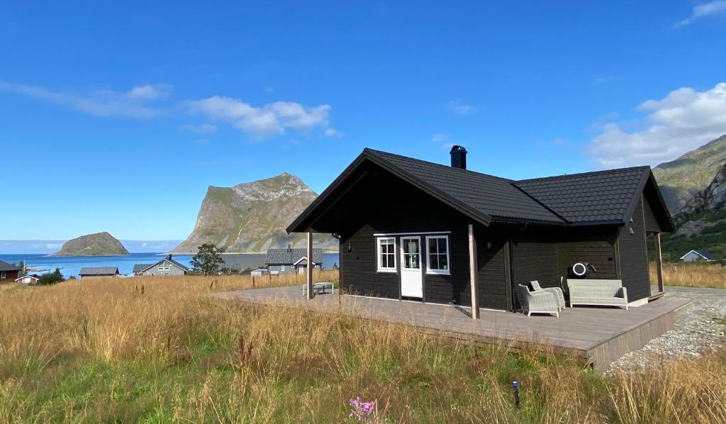 uma pequena casa preta com duas cadeiras brancas num deque em Tors Cabin at Haukland Beach em Offersøya
