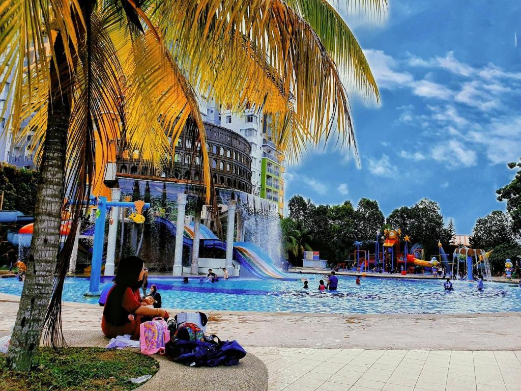 une femme assise sous un palmier devant un parc aquatique dans l'établissement Water Splashin Themepark Lagoon Resort Melaka City - By YouBNB Homestay Melaka, à Malacca
