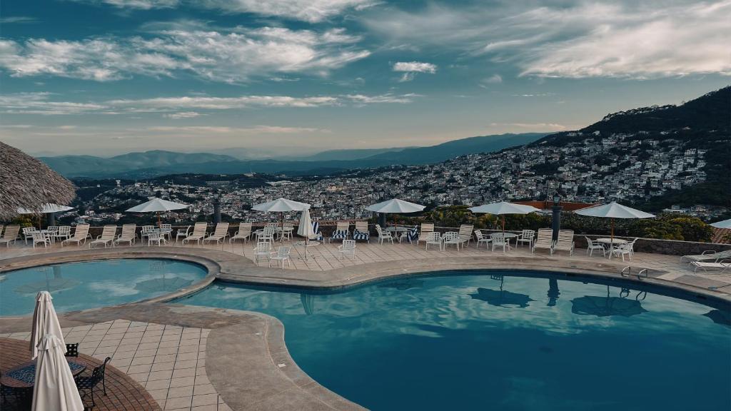 a swimming pool with tables and chairs and a city at Hotel Montetaxco in Taxco de Alarcón