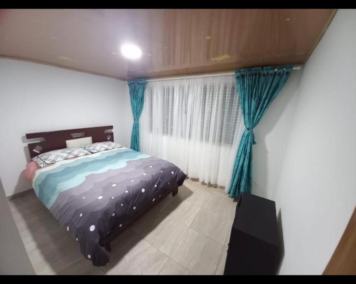 ein Schlafzimmer mit einem Bett und einem Fenster mit blauen Vorhängen in der Unterkunft Apartamento Familiar, cerca al Aeropuerto in Bogotá