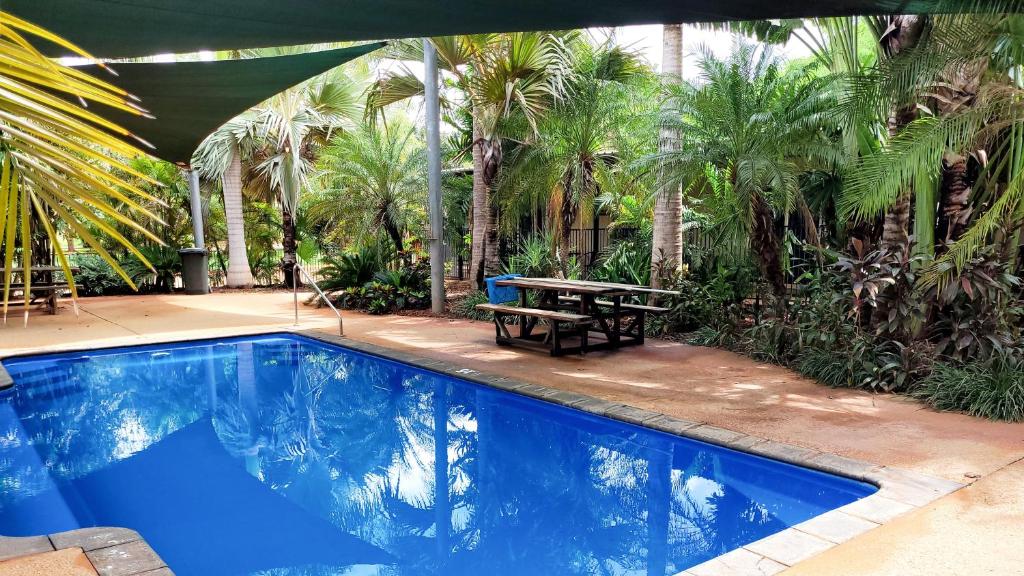 a swimming pool with a picnic table and palm trees at Roebuck Plains Roadhouse in Broome