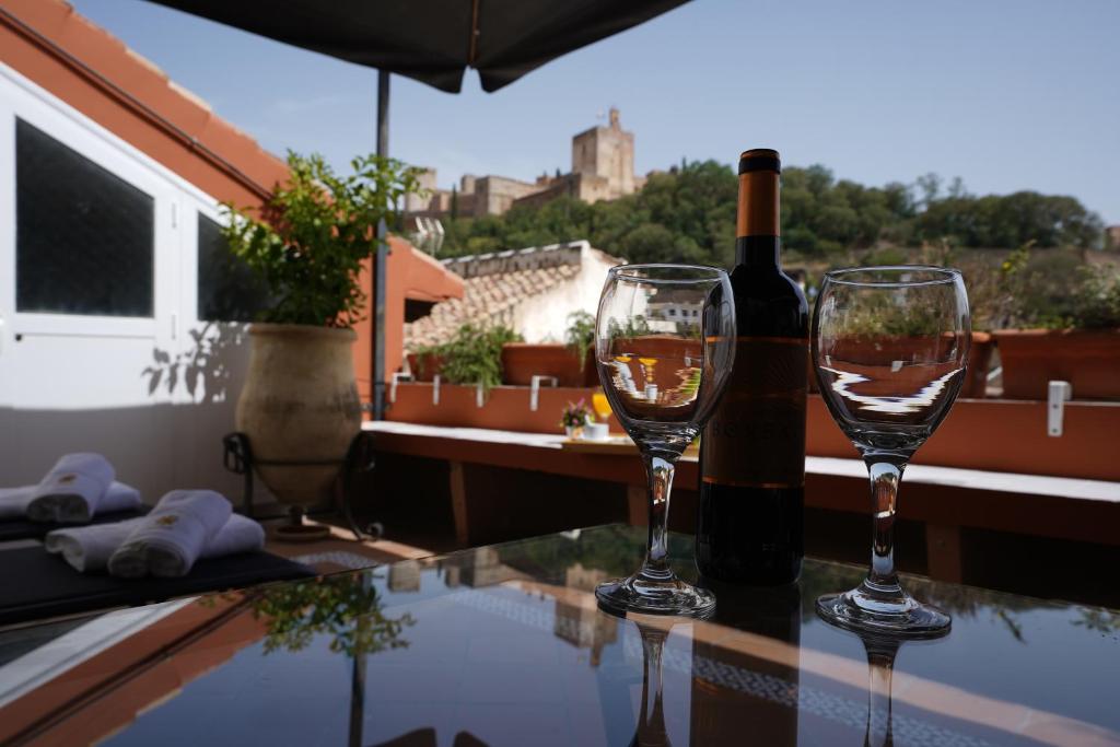 two wine glasses and a bottle of wine on a table at ADANAR-Apartamentos Muralla Zirí in Granada