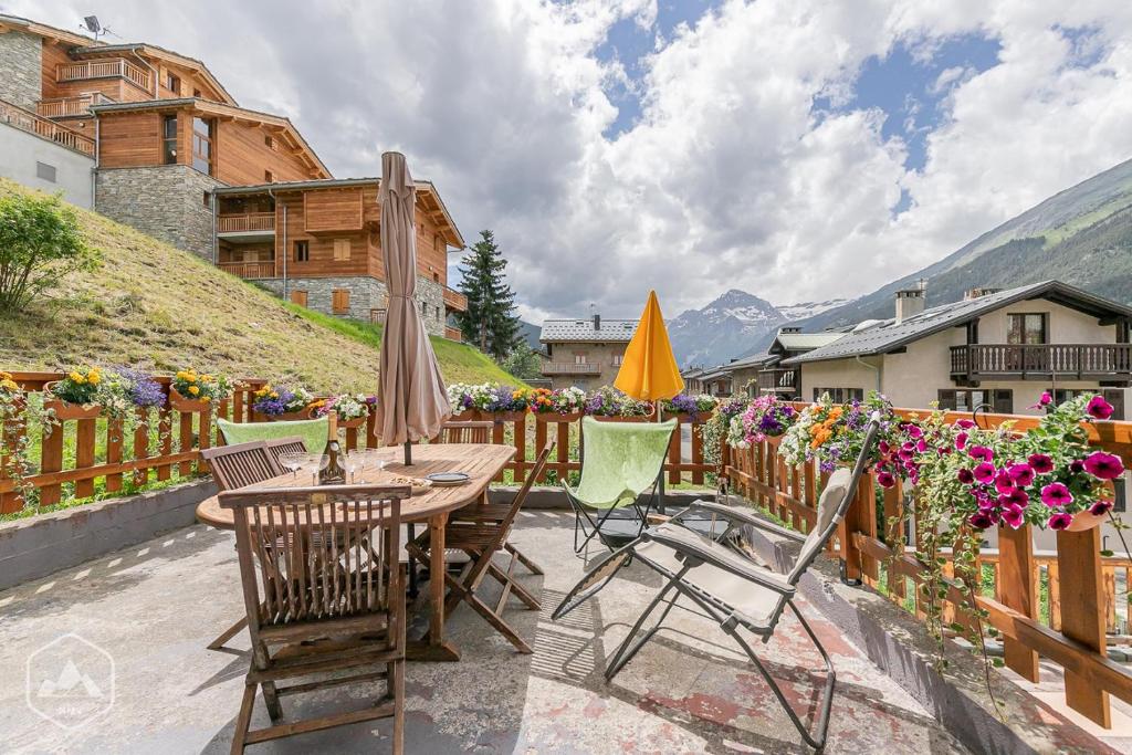 eine Terrasse mit einem Tisch, Stühlen und Blumen in der Unterkunft Locations Berne Milesi in Lanslevillard