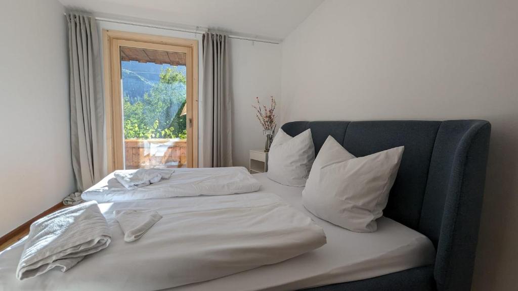 een bed met witte lakens en kussens en een raam bij Idyllisches Berg-Chalet mit Panoramablick in Bayrischzell