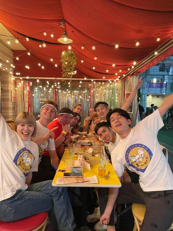 a group of people sitting at a table with their hands in the air at Sakura Hotel Ikebukuro in Tokyo