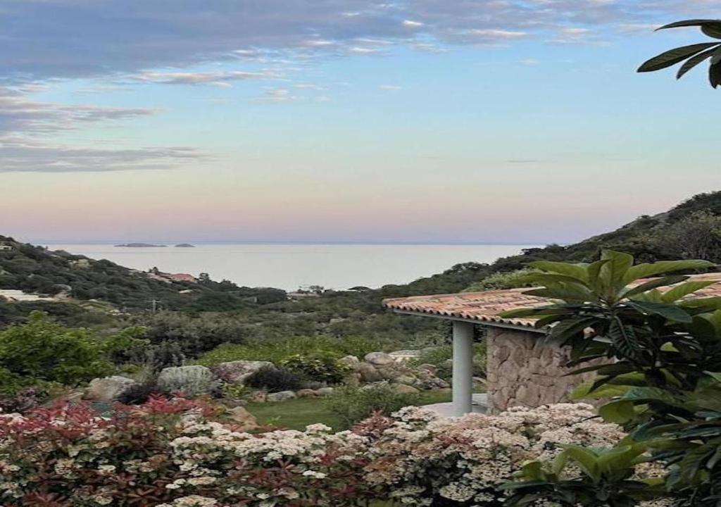 CORSACASA Villa in Palombaggia sea view في بورتو فيكيو: اطلالة على المياه من حديقة بها ورد