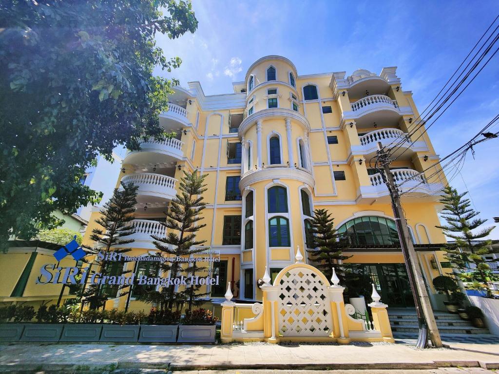 曼谷的住宿－Siri Ratchadamnoen Bangkok Hotel，一座黄色和白色的大建筑,前面有树木