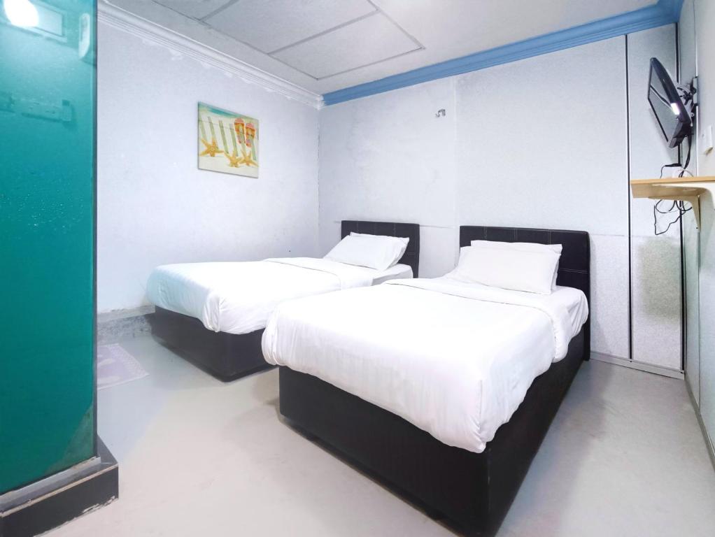 two beds in a hotel room with white sheets at Pen'U Cottages by RVH in Dungun