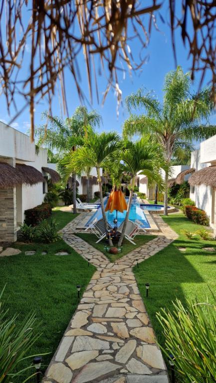 a resort yard with a swimming pool and palm trees at Oasis Tajaja Pousada in Jacumã