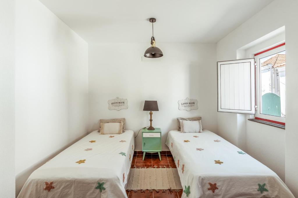 Duas camas num quarto com paredes brancas e uma janela em Pinheirinha Guest House em Alpiarça