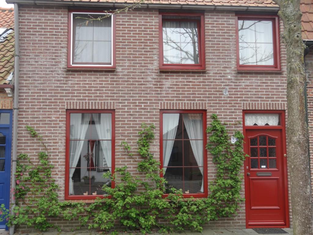 ein rotes Backsteinhaus mit vier Fenstern und einer roten Tür in der Unterkunft De Kersentuin Appartementen in Nieuwvliet