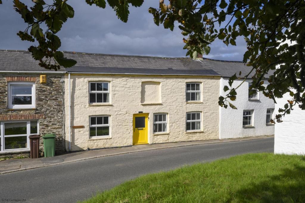 a stone house with a yellow door on a street at April Cottage in Saint Just in Roseland