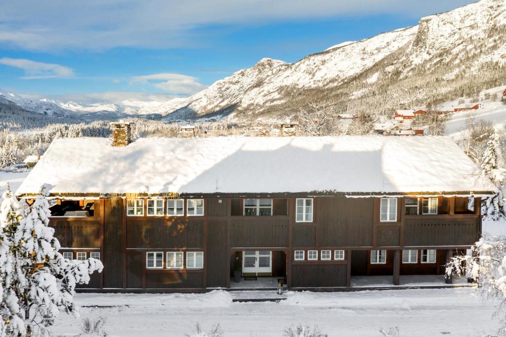 una casa cubierta de nieve con una montaña en el fondo en Villa Fredheim Farm, Hemsedal en Hemsedal