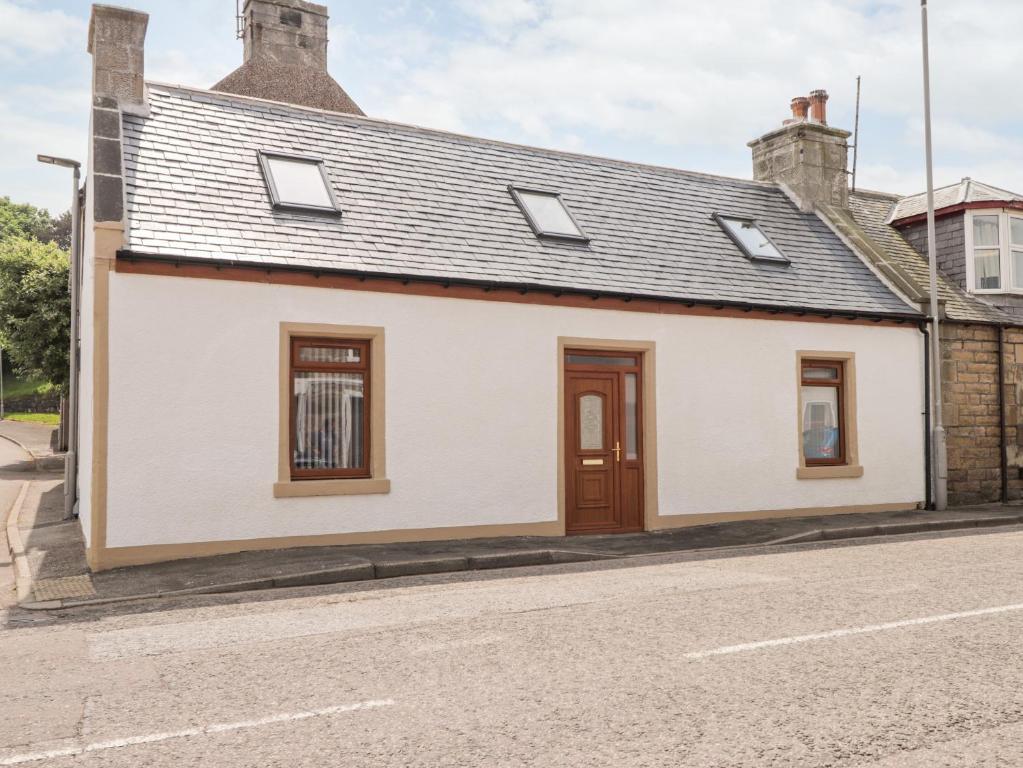 a white house with a brown door on a street at Corner Cottage in Buckie