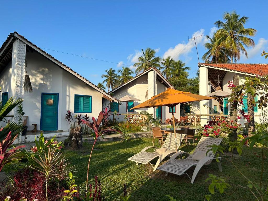 a house with a yard with chairs and an umbrella at Chalés Jardins dos Cajueiros in Tamandaré