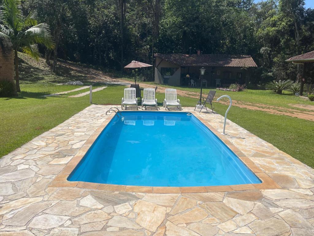 a swimming pool with two chairs and a table at Chalé Rio das Pedras in Santo Antônio do Pinhal