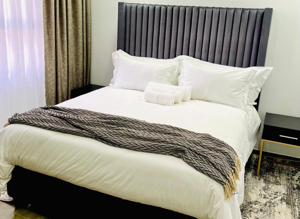 a bedroom with a large bed with white sheets and pillows at Mayswood Self Catering Apartments in Gaborone