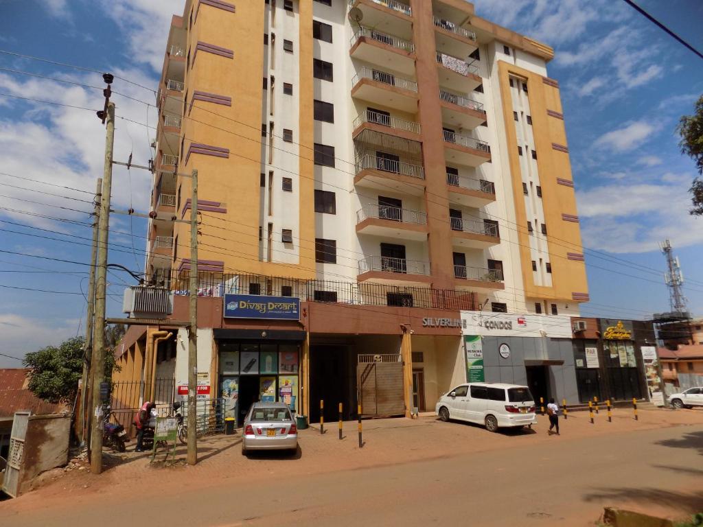 a tall yellow building with cars parked in front of it at Comfort Silverline Apartments in Kampala