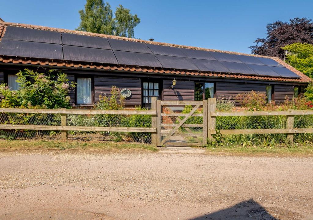a wooden house with a solar roof and a fence at The Cartshed at Farnham Barn 