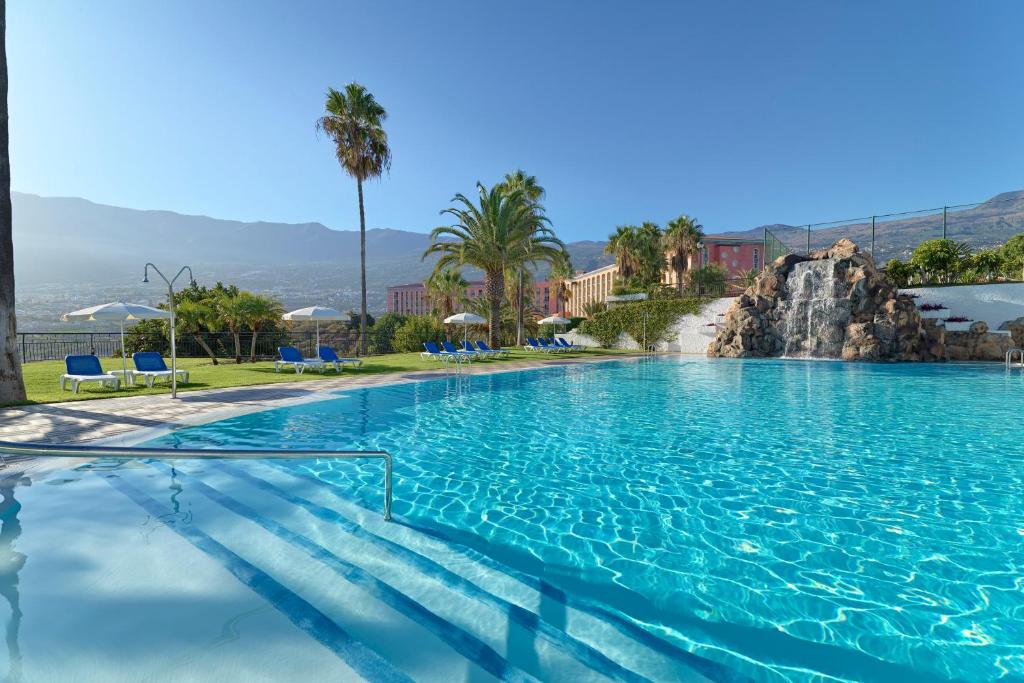 a large swimming pool with blue chairs and palm trees at Hotel Las Águilas Tenerife, Affiliated by Meliá in Puerto de la Cruz