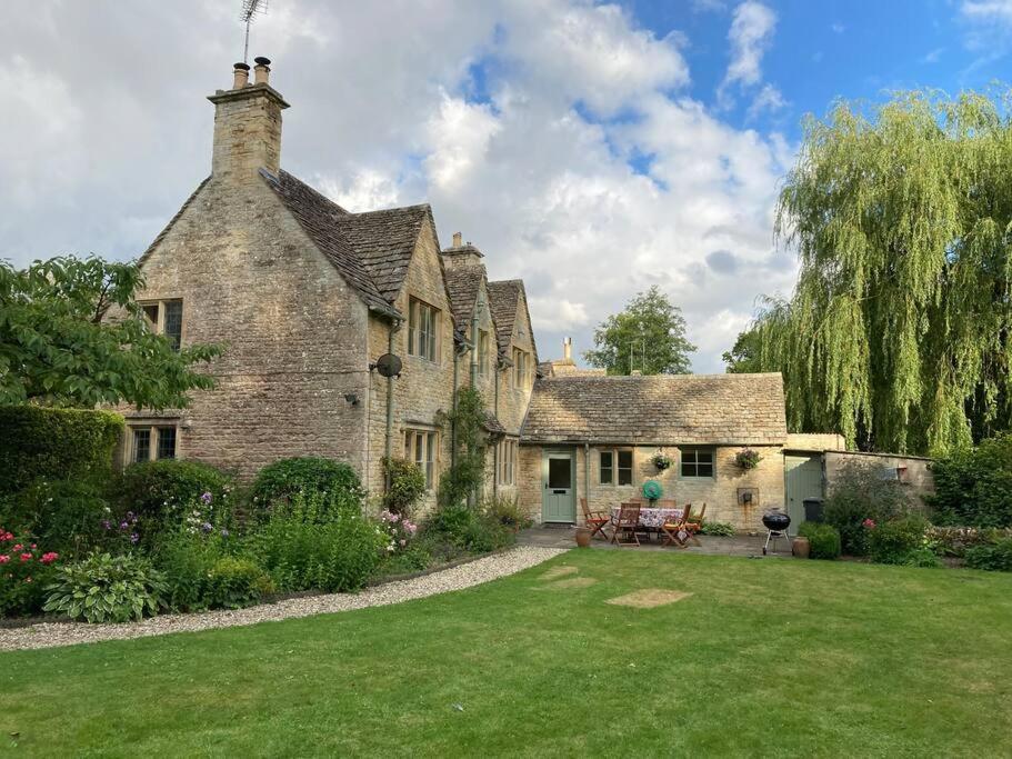 an old stone house with a lawn in front of it at Cotswolds Riverside Cottage in Bibury in Bibury