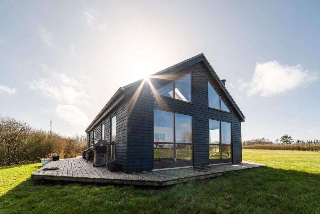 a black house with glass windows on a green field at Vidunderlig fritidshus ved Skov og Golfbane in Skjern