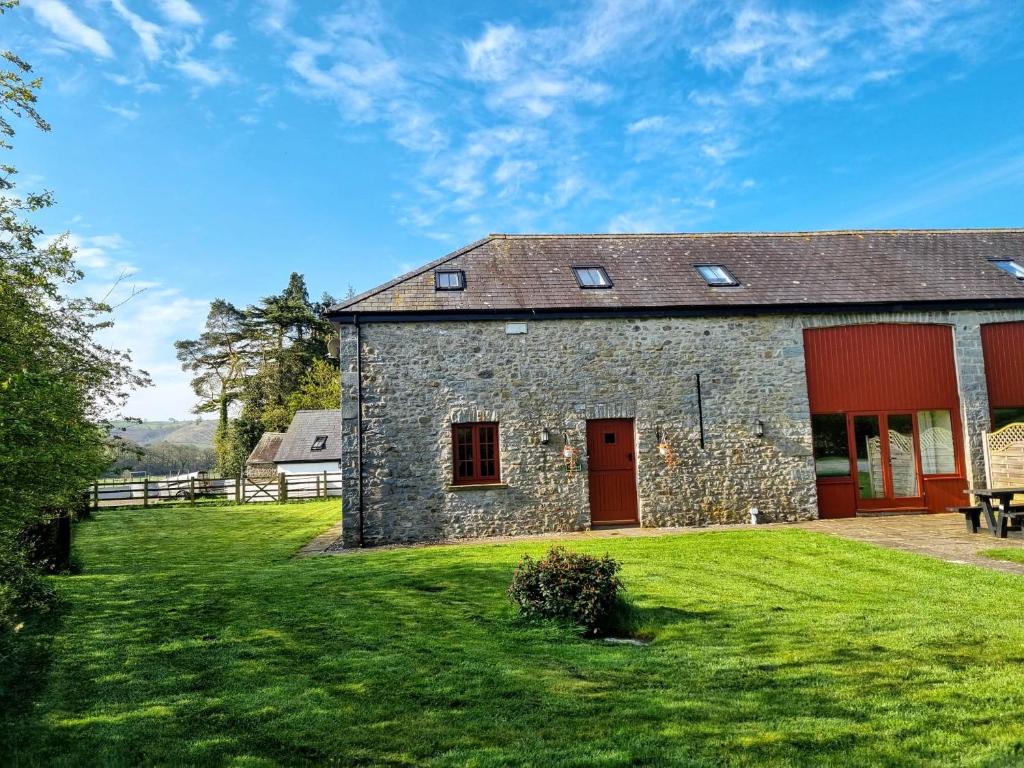 un edificio de piedra con puertas rojas y un patio verde en Peregrine Stable Cottage, en Llandovery