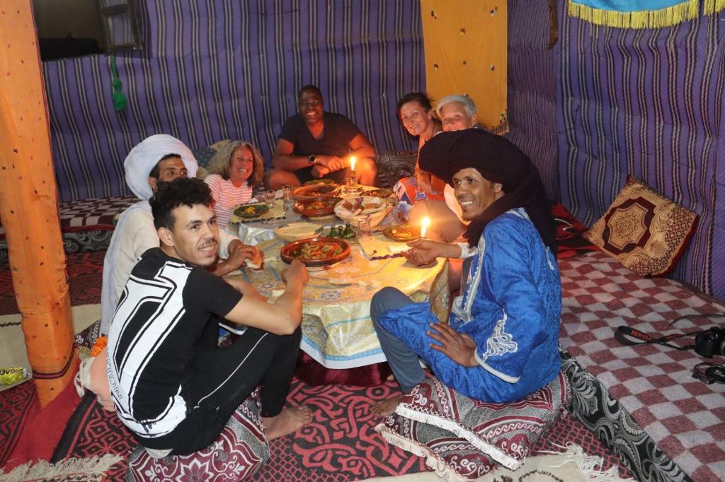 a group of people sitting around a table eating at Sahara Berber Camp - Mhamid Discovery Camp in Mhamid el Rhozlane