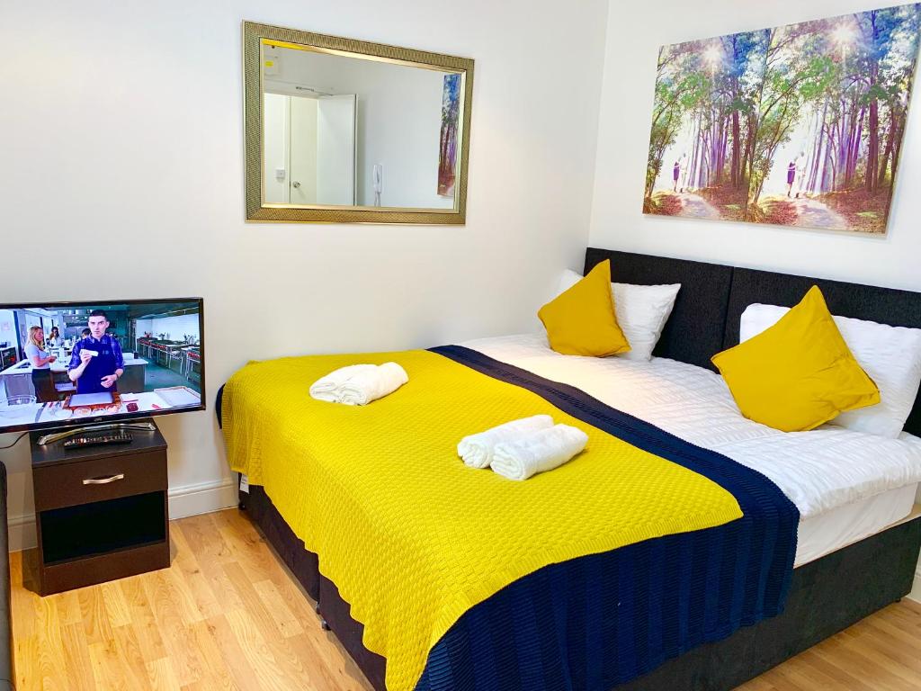 Cette chambre dispose de 2 lits, d'une télévision et d'une couverture jaune. dans l'établissement London Studio Apartments Close to Station NP5, à Londres