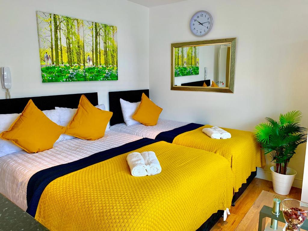 two beds in a room with yellow sheets and a mirror at London Studio Apartments Close to Station NP6 in London