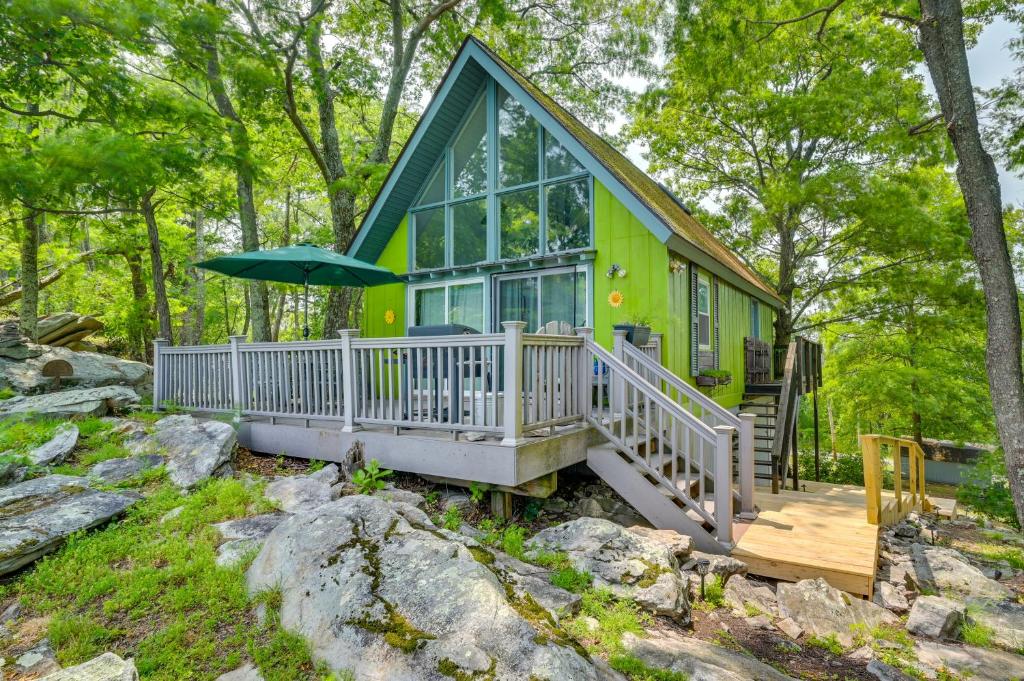 una casa verde con porche y sombrilla en Cozy Great Cacapon Cabin with Mountain Views, en Great Cacapon