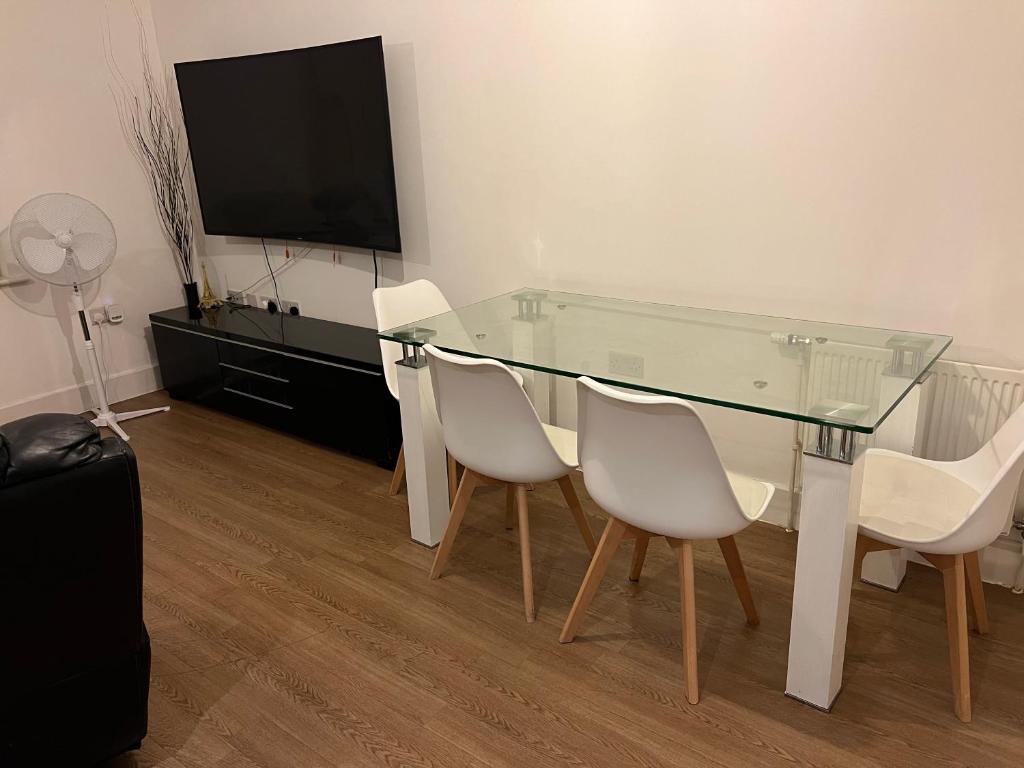 tavolo da pranzo in vetro con sedie bianche e TV a schermo piatto di Comfy One bedroom Apartment a Londra