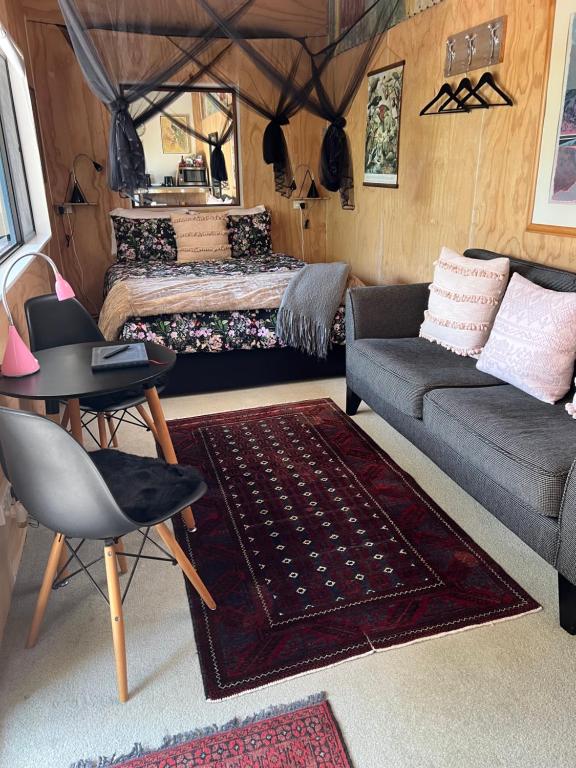 uma sala de estar com um sofá, uma cama e uma mesa em Kākā Ridge Retreat Bush Hideaway em Tawharanui