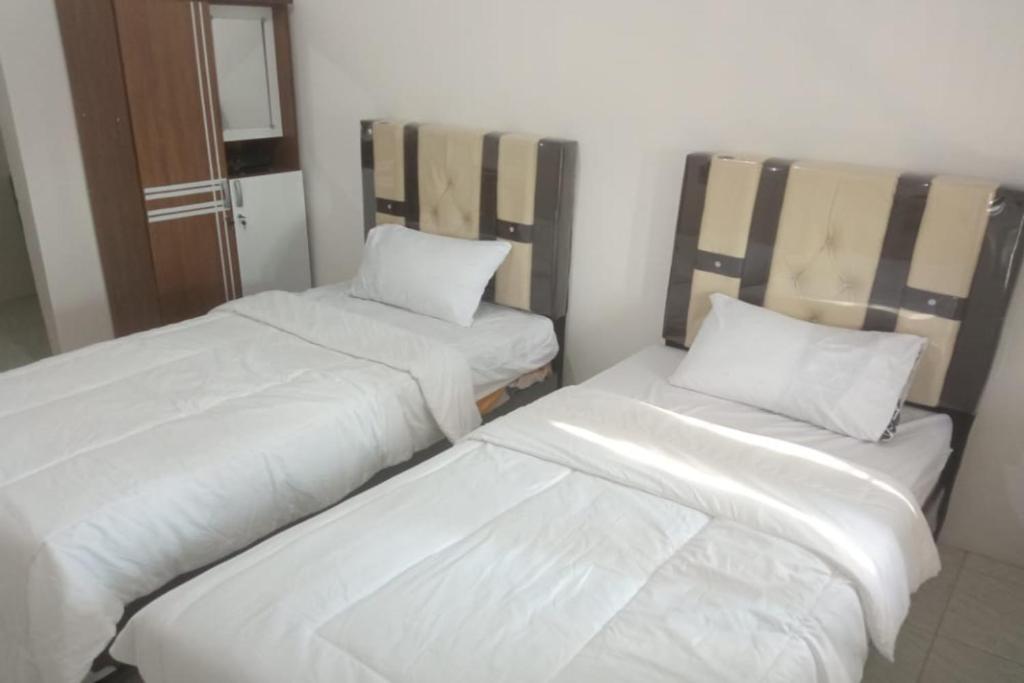 two beds in a room with white sheets and pillows at OYO 93100 Harapan Homestay Syariah in Parit