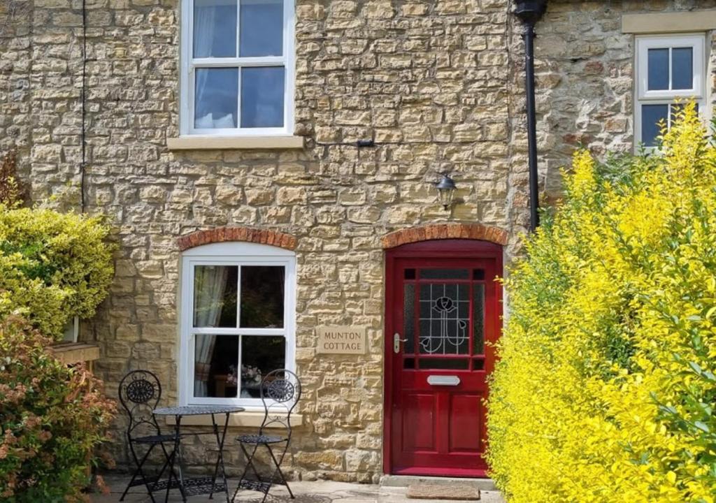 una casa de ladrillo con una puerta roja y una mesa en Munton Cottage, en Crakehall