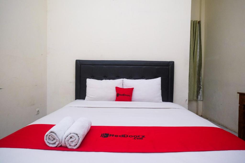 a bedroom with a red and white bed with two towels at RedDoorz Syariah at Griya Hanum Condoongcatur in Kejayan