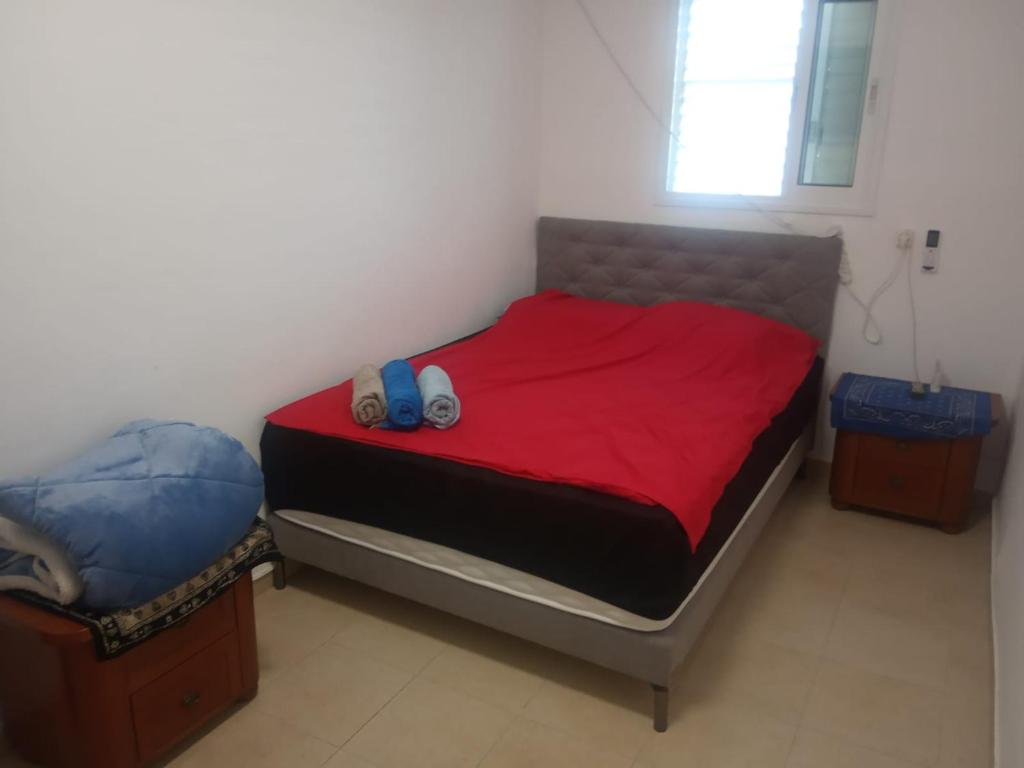 um quarto com uma cama com lençóis vermelhos e 2 chinelos em דירת שי em Rishon LeZion