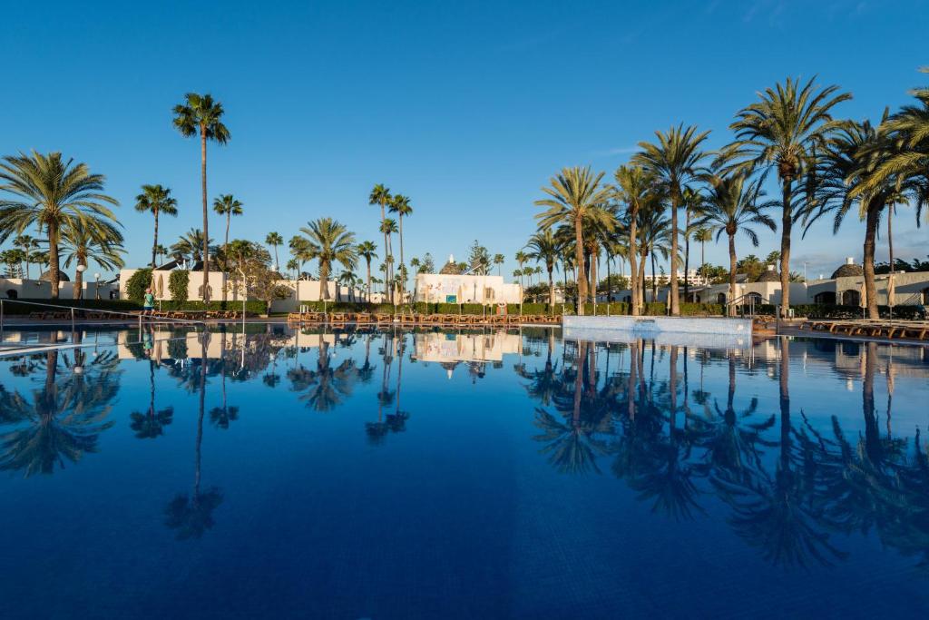 a swimming pool with palm trees and a blue sky at HD Parque Cristobal Gran Canaria in Playa del Ingles