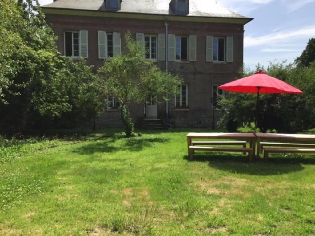 two park benches with an umbrella in front of a house at Le Clos du bas hameau in Canouville