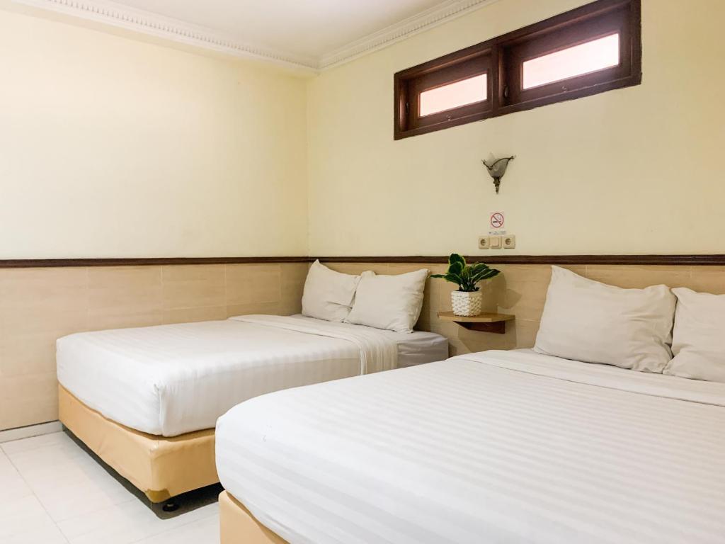 two beds in a room with white walls and windows at Musafira Hotel Syariah Malioboro Yogyakarta Mitra RedDoorz in Yogyakarta