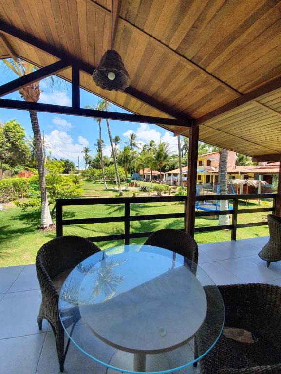 Una mesa de cristal y sillas bajo un techo de madera. en Chalé em Maragogi, en Maragogi